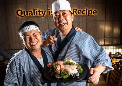 portrait of two japanese chefs with a plate of sushi laughing